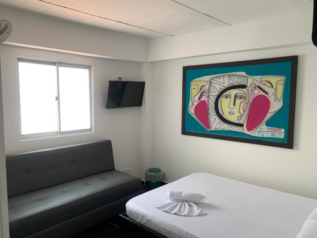 A hotel room with a bed, a bench, a television, and a window.