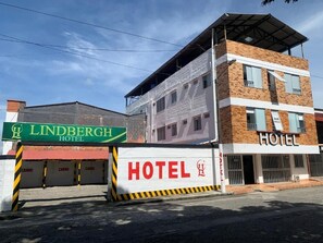 Un hotel con un cartel llamativo, una zona de estacionamiento techada y un edificio con un ventanal visible.