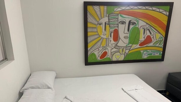 Ein Einzelbett mit weißer Bettwäsche, ein Bild darüber und ein kleiner Nachttisch.