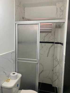 A bathroom with a shower enclosure, a toilet, and a marble-tiled wall. - Hotel Lindbergh Quindio (Armenia)
