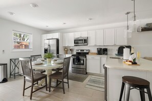 A modern kitchen with white cabinets, stainless steel appliances, and a dining area with a glass table and chairs. - Lowcountry Retreat | Minutes to Everything! (Mt Pleasant)