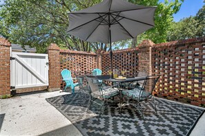 An outdoor patio with a table and chairs, a brick wall, and a white gate. - Lowcountry Retreat | Minutes to Everything! (Mt Pleasant)