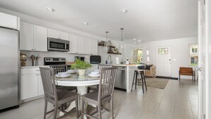 A modern kitchen with white cabinets, stainless steel appliances, and a dining area with a glass table and wooden chairs. - Lowcountry Retreat | Minutes to Everything! (Mt Pleasant)