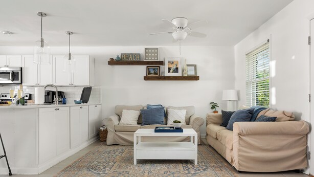 A modern living room with a sofa, coffee table, and a kitchen area with cabinets and appliances. - Lowcountry Retreat | Minutes to Everything! (Mt Pleasant)