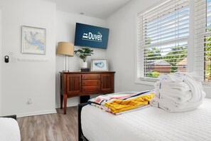 A hotel room with a bed, a TV, a map, a plant, and a window with blinds. - Lowcountry Retreat | Minutes to Everything! (Mt Pleasant)
