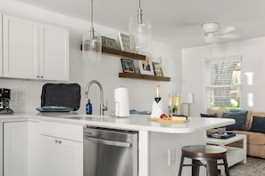 Uma cozinha moderna com armários brancos, uma máquina de lavar louça, uma cafeteira e um espaço de jantar com mesa posta para refeição.
