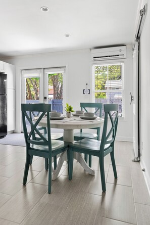A modern kitchen with a dining area, featuring a round table with chairs, a built-in oven, and a window with blinds. - Coastal Townhouse | Minutes from Everything (Mt Pleasant)