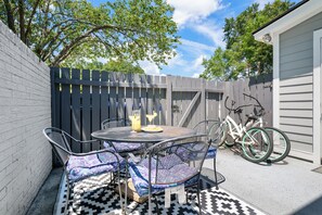 An outdoor patio with a round table and chairs, a bicycle, and a fence. - Coastal Townhouse | Minutes from Everything (Mt Pleasant)