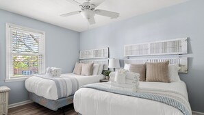 Ein Schlafzimmer mit zwei Betten, einem Deckenventilator und einem Fenster mit Jalousien.