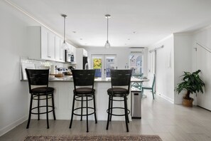 A modern kitchen with white cabinets, a central island with bar stools, pendant lighting, and a view of the outdoors. - Coastal Townhouse | Minutes from Everything (Mt Pleasant)