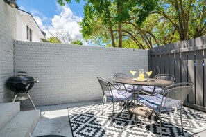 A patio with a round table and chairs, a grill, and a patterned rug. - Coastal Townhouse | Minutes from Everything (Mt Pleasant)