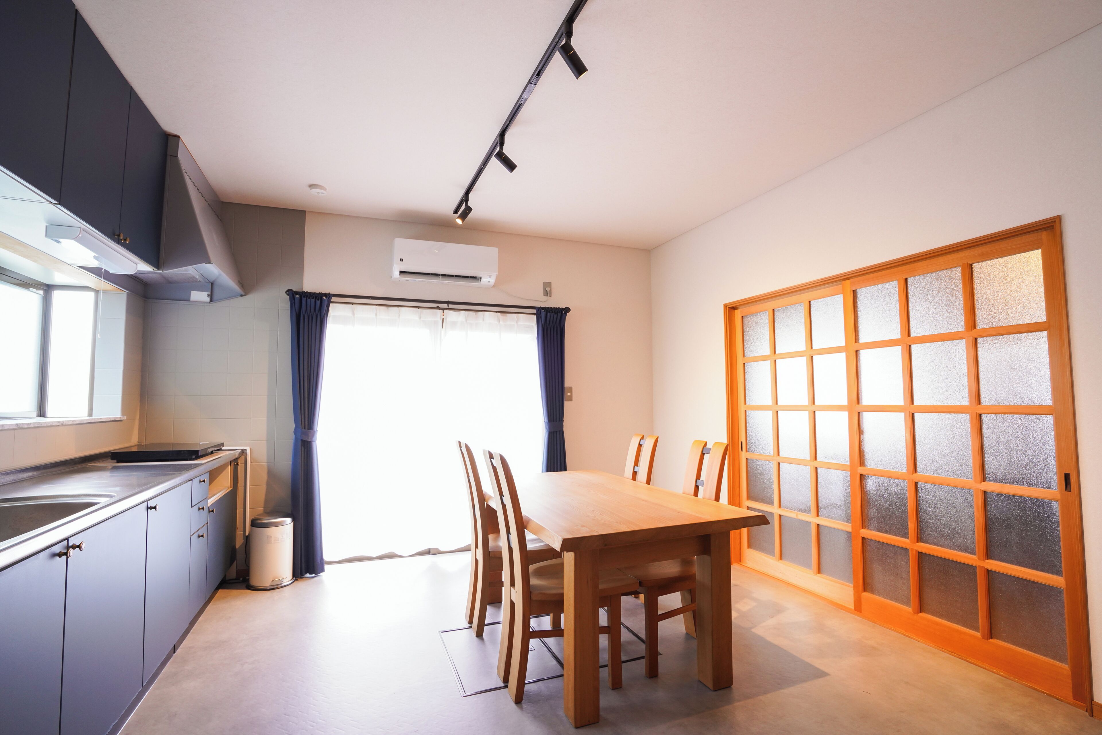 Cocina compacta con comedor, que incluye una mesa, sillas, un ventanal con cortinas y un equipo de aire acondicionado.