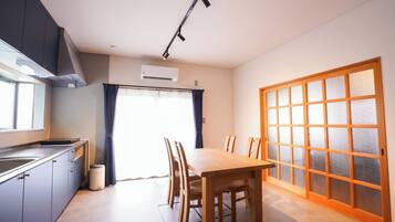Cocina compacta con comedor, que incluye una mesa, sillas, un ventanal con cortinas y un equipo de aire acondicionado.