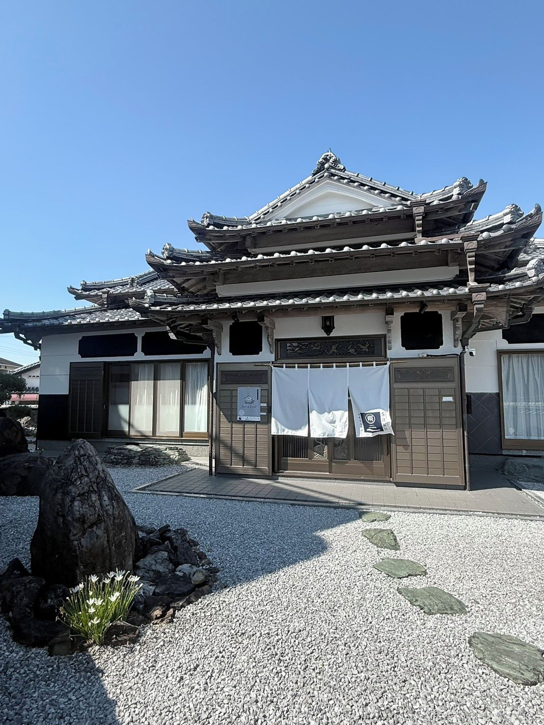 A traditional Japanese building with a tiled roof, a wooden entrance gate, and a gravel pathway.