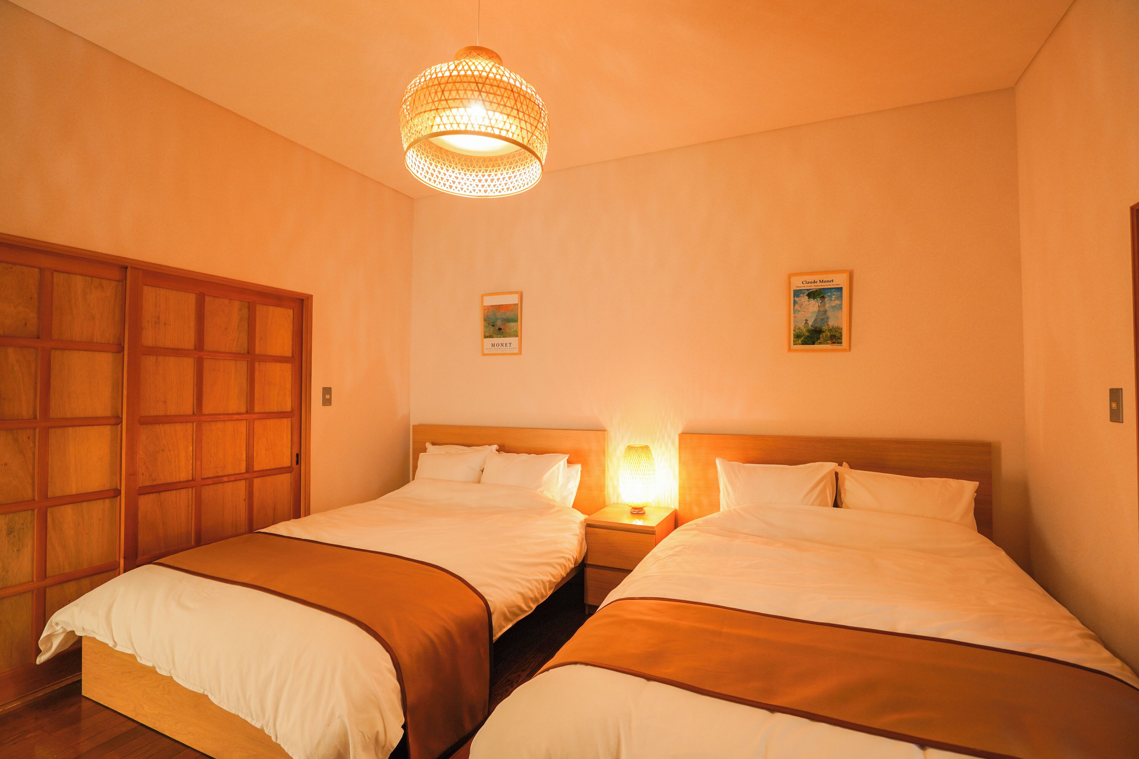 A hotel room with two beds, a wooden wardrobe, and a hanging light fixture.