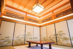 A traditional Japanese room with tatami flooring, sliding doors, and a wooden ceiling with intricate carvings.