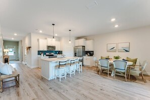 A modern kitchen with white cabinetry, a central island with bar stools, and a dining area with wicker chairs. - SnowBirds Welcome| Low Rates WindMark| Golf Cart + Game Garage Retreat (Port St. Joe)