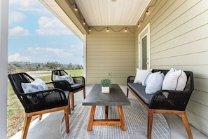 An outdoor patio with a table and two sofas, a potted plant, and a view of a grassy area. - Low Rates WindMark| Golf Cart + Game Garage Retreat (Port St. Joe)