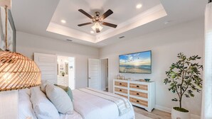 A bedroom with a bed, a ceiling fan, a dresser, a television, and a plant. - Low Rates WindMark| Golf Cart + Game Garage Retreat (Port St. Joe)