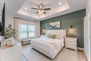 Un dormitorio con cama, mesitas de noche, ventilador de techo y ventana con cortinas.