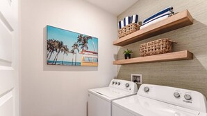 A laundry room with a washing machine, a dryer, and a wall-mounted shelf with baskets. - Low Rates WindMark| Golf Cart + Game Garage Retreat (Port St. Joe)