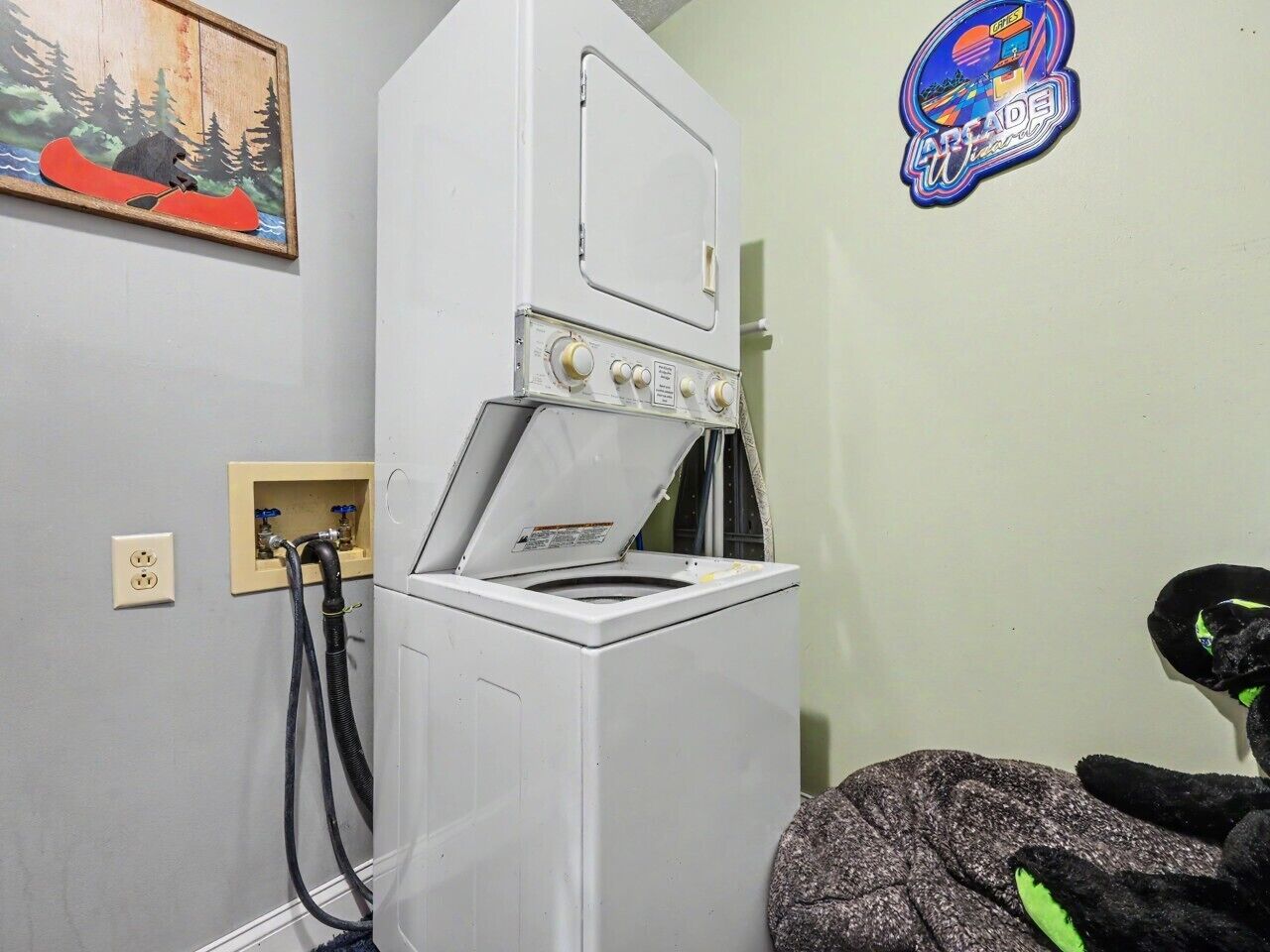 Een kleine kamer met een witte wasmachine, een stopcontact en een sticker op de muur.