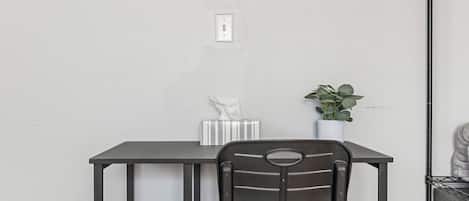 A compact workspace with a desk and chair, a framed painting on the wall, and a potted plant.