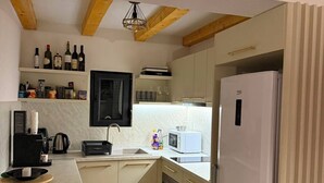 A modern kitchen with white cabinets, a built-in oven, a microwave, and a refrigerator. There is a wooden ceiling with exposed beams, and a shelf with bottles.
