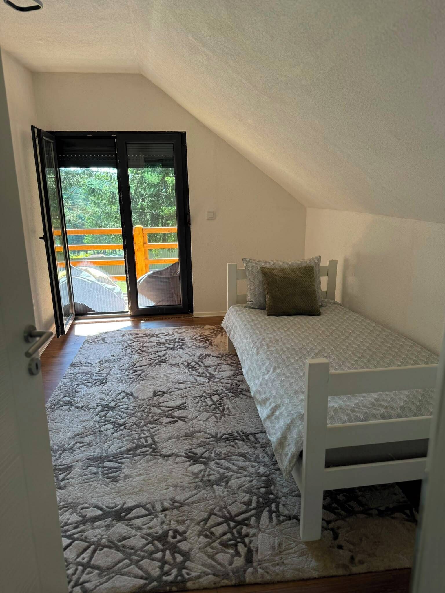 A small, single-bed room with a sloped ceiling and a view through a glass door to an outdoor area.