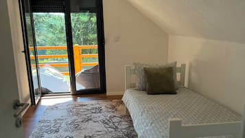 A small, single-bed room with a sloped ceiling and a view through a glass door to an outdoor area.