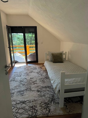 A small, single-bed room with a sloped ceiling and a view through a glass door to an outdoor area.