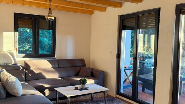 A modern living room with a grey sofa, a white coffee table, and a shaggy rug. There are large windows and a view of the outdoors.