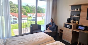 Una habitación de hotel con cama, una silla, escritorio, cafetera y televisión.
