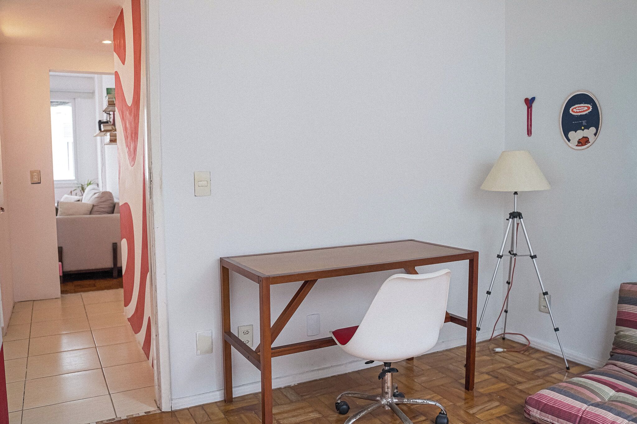 A room with a wooden desk, a white chair, a lamp, and a striped sofa.