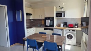 Una cucina compatta con forno a microonde, forno, macchina per il caffè, un tavolo da pranzo con sedie e una lavatrice.
