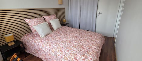 A neatly made bed with a patterned bedspread, a bedside table with a lamp, and a window with curtains.