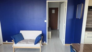 Una stanza con una parete blu, un divano bianco con cuscini azzurri, una porta in legno e una scala.