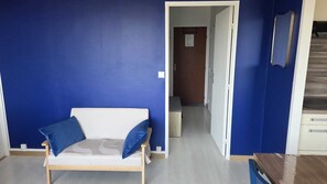 A room with a blue wall, a white sofa with blue cushions, a wooden door, and a staircase. - Appartement rénové et lumineux à 50 mètres de la mer et de la promenade. (Cabourg)