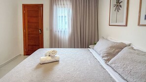 A hotel room with a bed, a door, a window with curtains, and a framed picture on the wall.