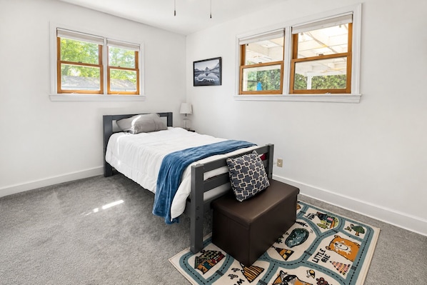 A bedroom with a bed, a nightstand, a lamp, a window, and a rug.