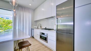 A modern kitchen with white cabinetry, a stainless steel refrigerator, a built-in oven, and a dining area with a bar stool.