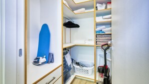 Ein Schrank mit Regalen, einer Kleiderstange und einem Staubsauger.