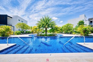 A swimming pool with a no diving sign, surrounded by palm trees and modern buildings. - Lush Oasis in the heart of 7mile Beach Area (George Town)