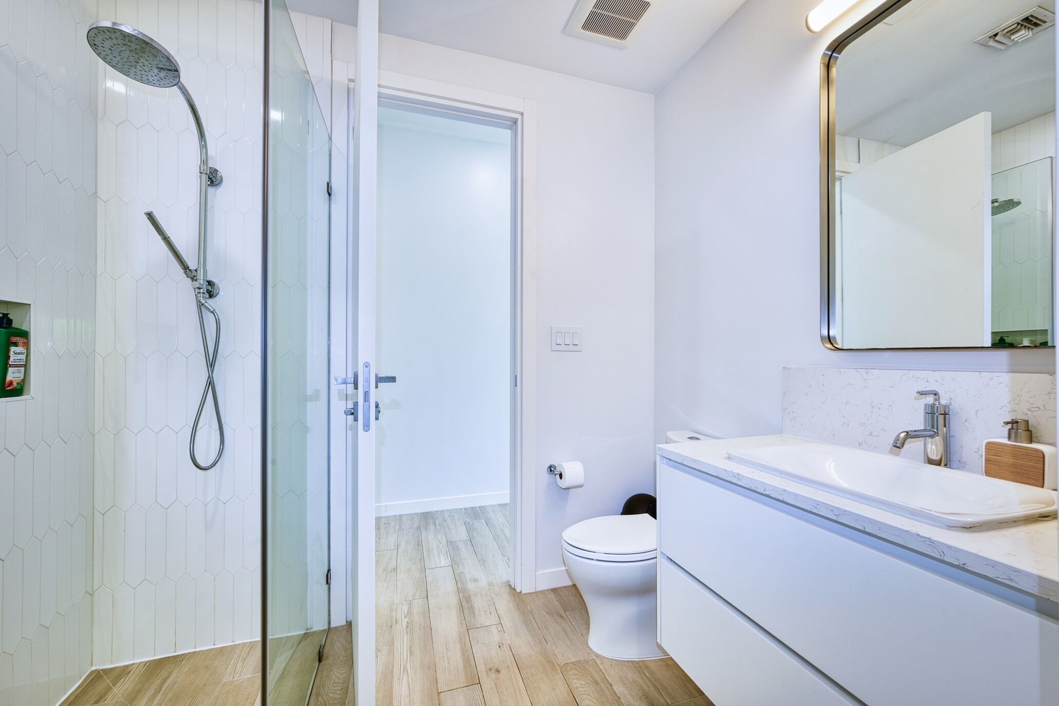 A modern bathroom with a glass-enclosed shower, a toilet, and a sink with a mirror above it.