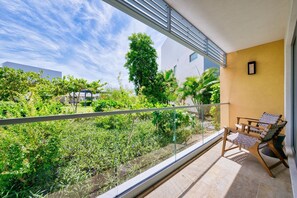 A balcony with a glass railing, a chair, and a table. - Lush Oasis in the heart of 7mile Beach Area (George Town)
