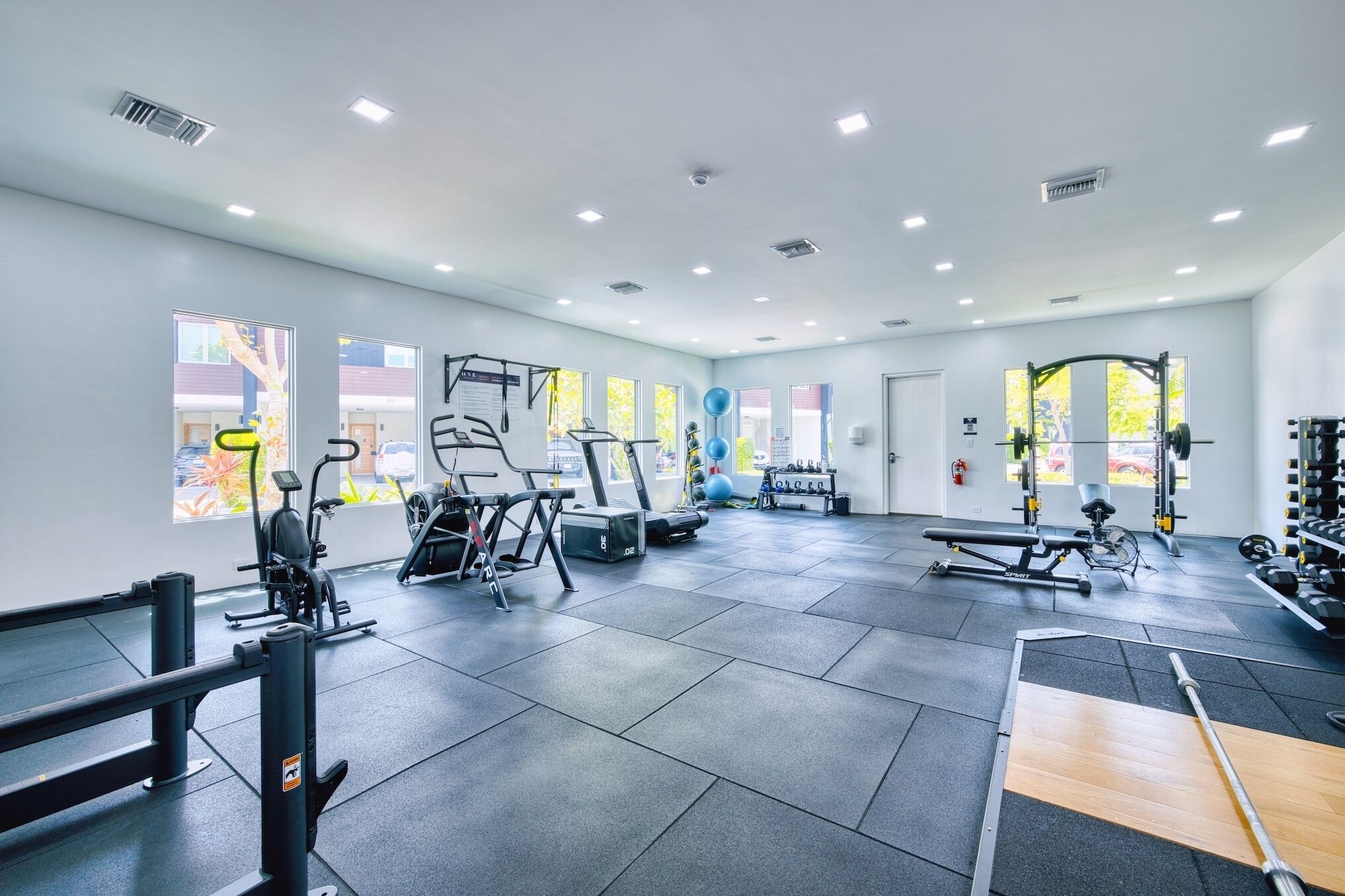 Une salle de sport équipée de divers appareils d’exercice, dotée de grandes fenêtres et présentant un design moderne et épuré.