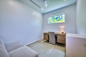 A modern room with a desk, chair, and a view of greenery through a window. - Lush Oasis in the heart of 7mile Beach Area (George Town)