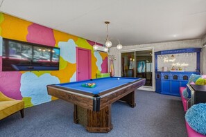 A room with a pool table, colorful walls, a television, and a blue cabinet with a neon sign. - Casa Calliandra | Pool, Spa & Game Room (Palm Springs)