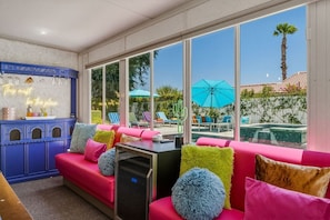 A modern lounge area with a pool view, a neon sign, and a blue cabinet. - Casa Calliandra | Pool, Spa & Game Room (Palm Springs)