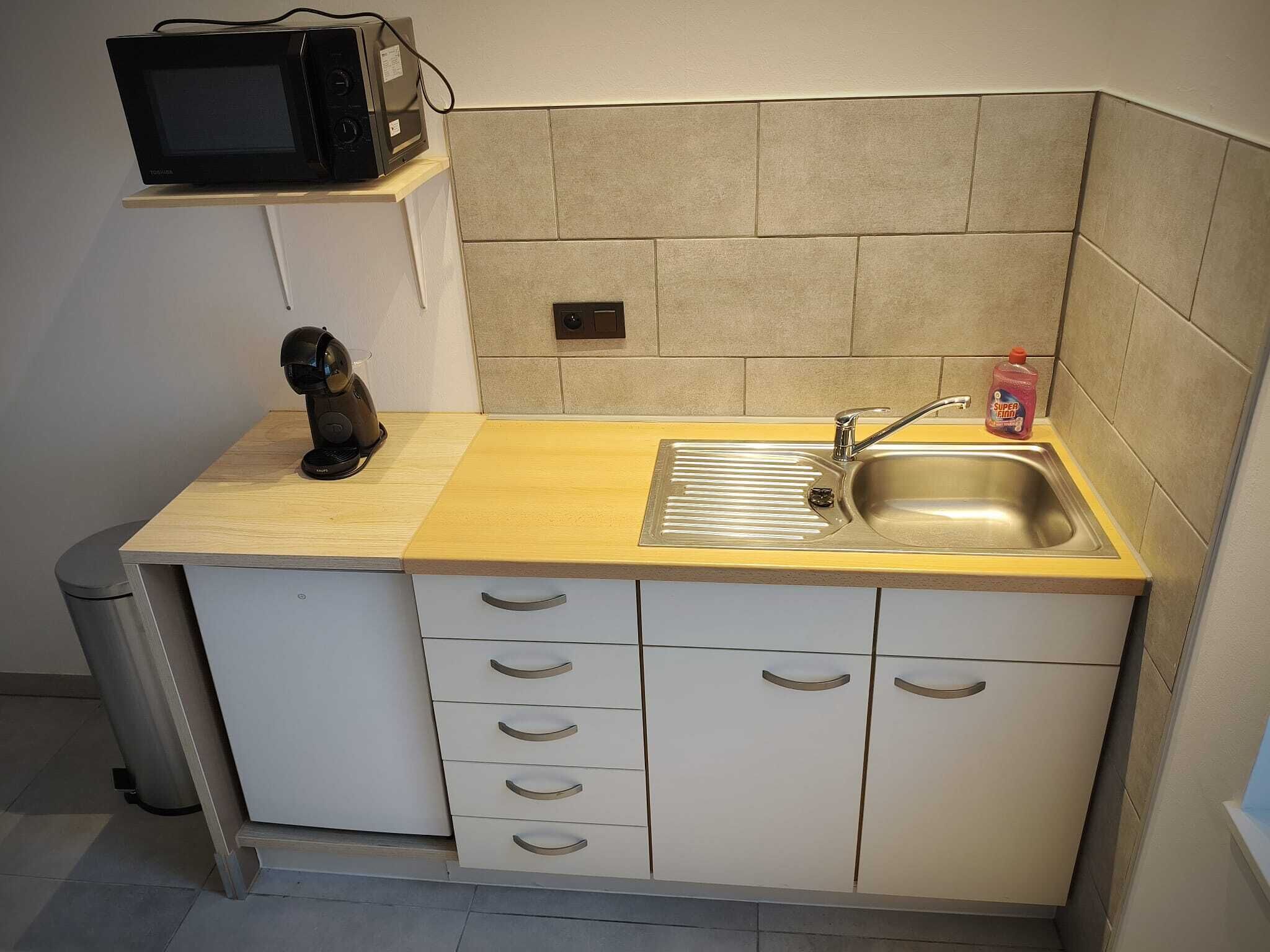A compact kitchen with a microwave, coffee machine, sink, and a small cabinet.